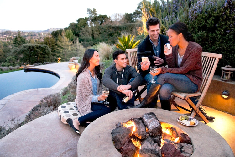 Diverse group of people sitting around campfire by the pool, having drinks and woman blowing into a breathalyzer